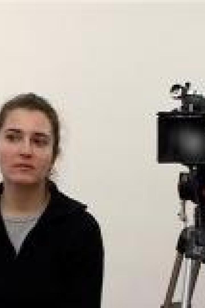 Eine Frau sitzt vor einer Kamera und einem Scheinwerfer.