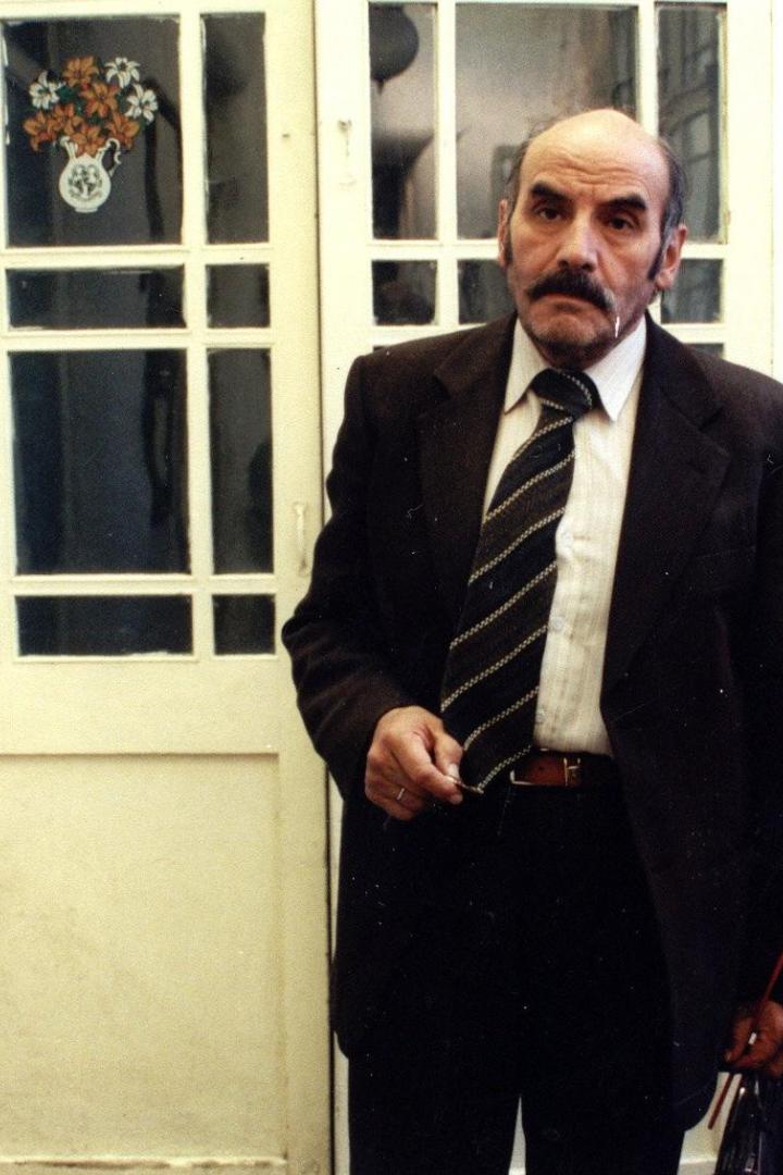 Ein Mann mit Anzug und rotem Herzluftballon steht vor einer Tür.