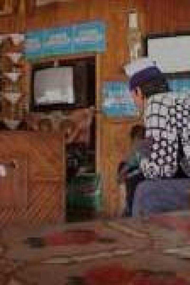 Ein Mann mit Mütze sitzt in einem kleinen Raum mit Fernseher.