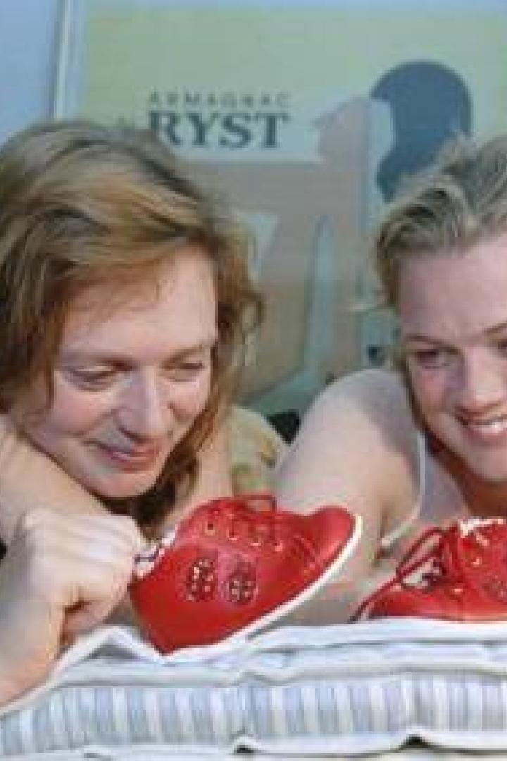 Zwei Frauen betrachten lächelnd rote Babyschuhe auf einem Bett.