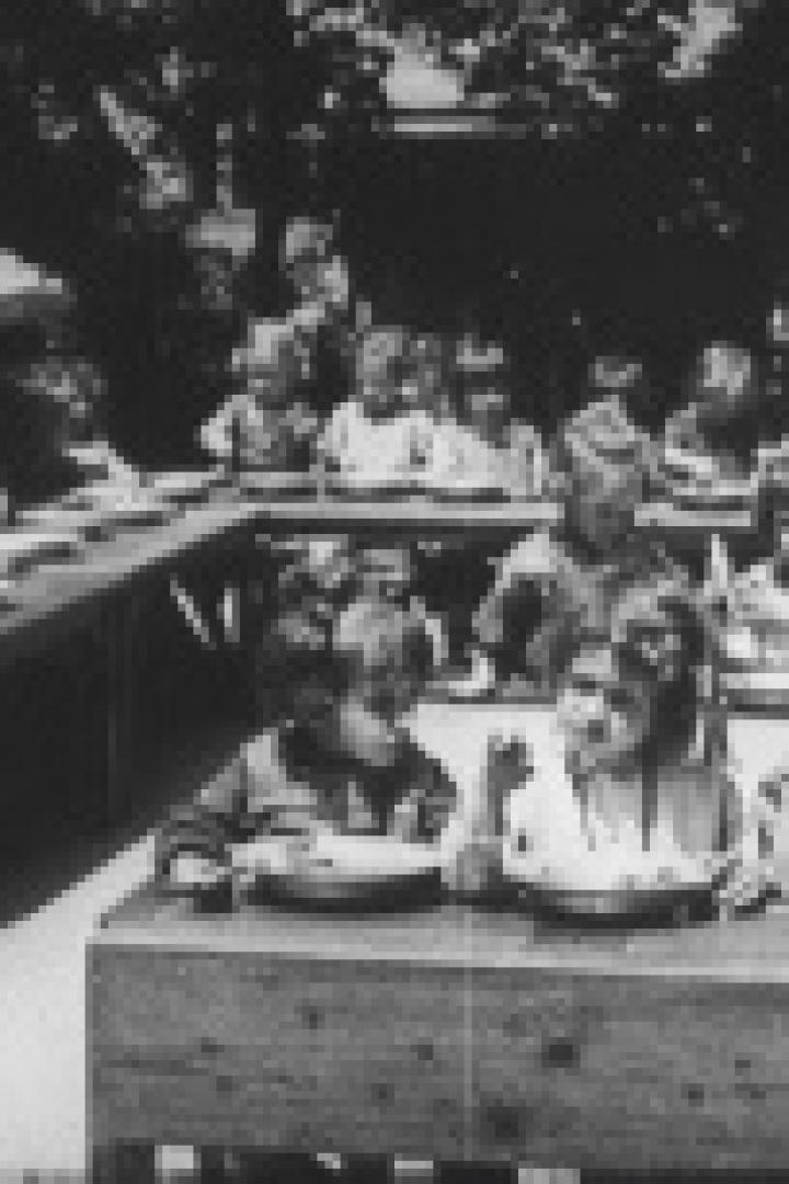 Eine Gruppe von Kindern sitzt an Tischen und isst in einer Art Freiluft-Cafeteria.