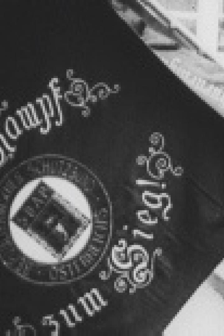 Eine schwarz-weiße Aufnahme einer Fahne mit der Aufschrift „Durch Kampf zum Sieg!“.