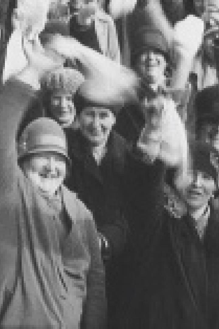 Eine Menschenmenge in Hüten und Mänteln winkt und jubelt.