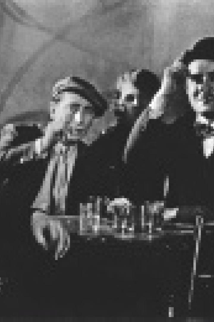 Eine Gruppe von Menschen sitzt an einem Tisch mit Schnapsgläsern in einem verrauchten Raum.