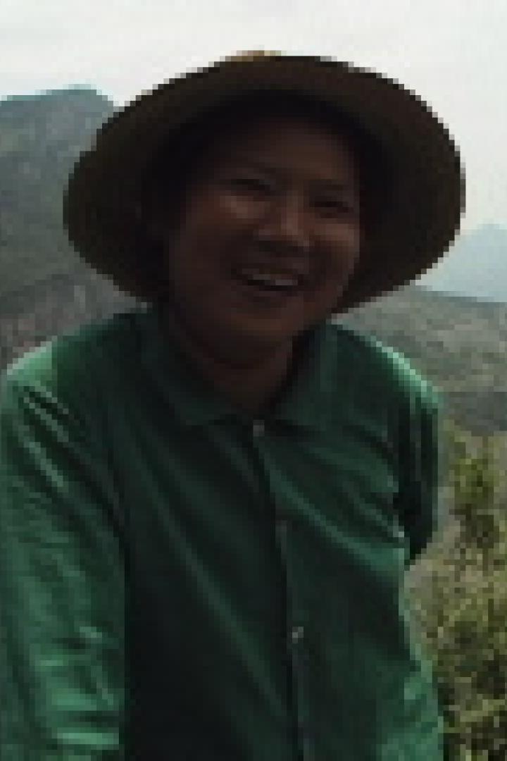 Eine lächelnde Frau mit Hut steht vor einer Berglandschaft.