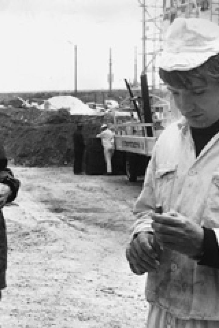 Zwei Männer stehen auf einer Baustelle, einer im Anzug, der andere in Arbeitskleidung.