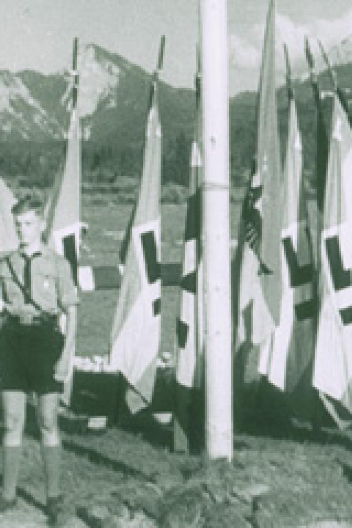 Zwei Jungen in Uniform stehen vor einer Reihe von Flaggen mit Hakenkreuzen.