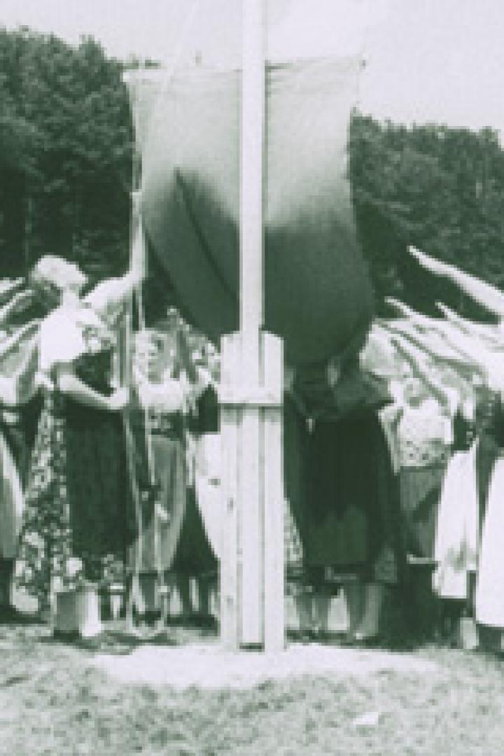 Eine Gruppe junger Frauen in Tracht salutiert vor einem Fahnenmast.