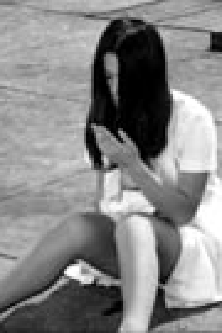 Eine junge Frau sitzt auf dem Boden und schaut auf ihre Hände.