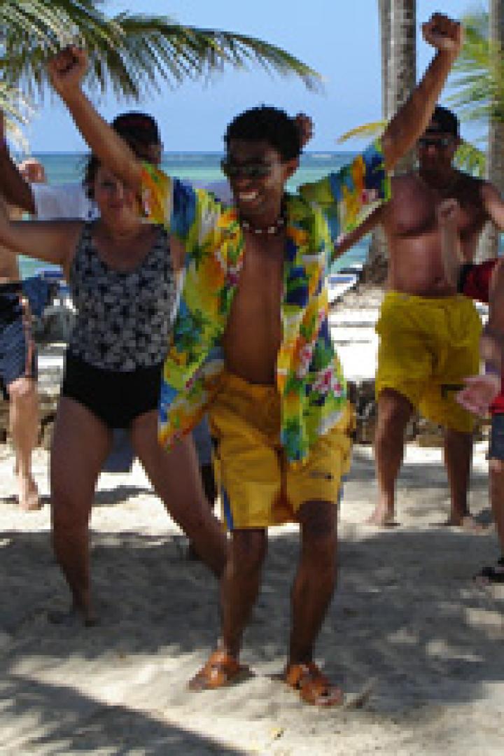 Eine Gruppe von Menschen tanzt am Strand unter Palmen.