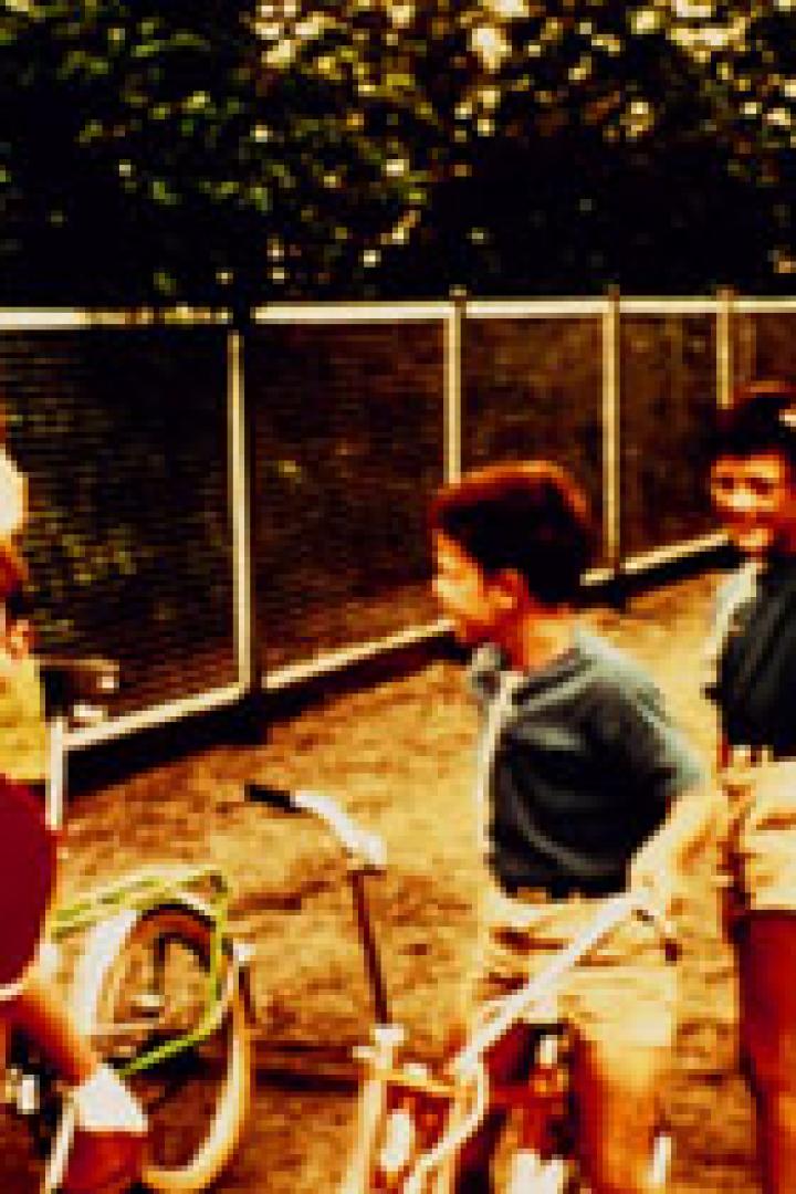 Eine Gruppe Kinder steht und spielt im Freien neben einem Fahrrad.