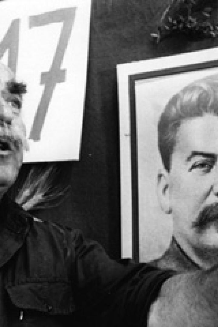 Ein Mann mit Schnurrbart gestikuliert vor einem Porträt von Stalin.