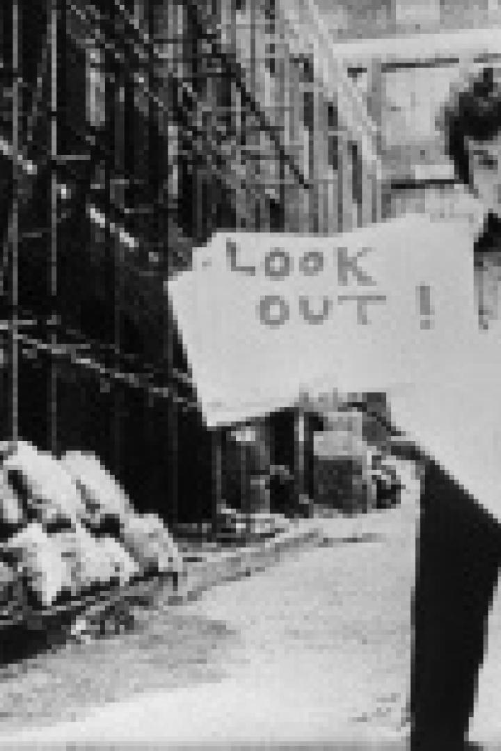 Ein Mann hält ein Schild mit der Aufschrift „Look Out!“ in einer Gasse.