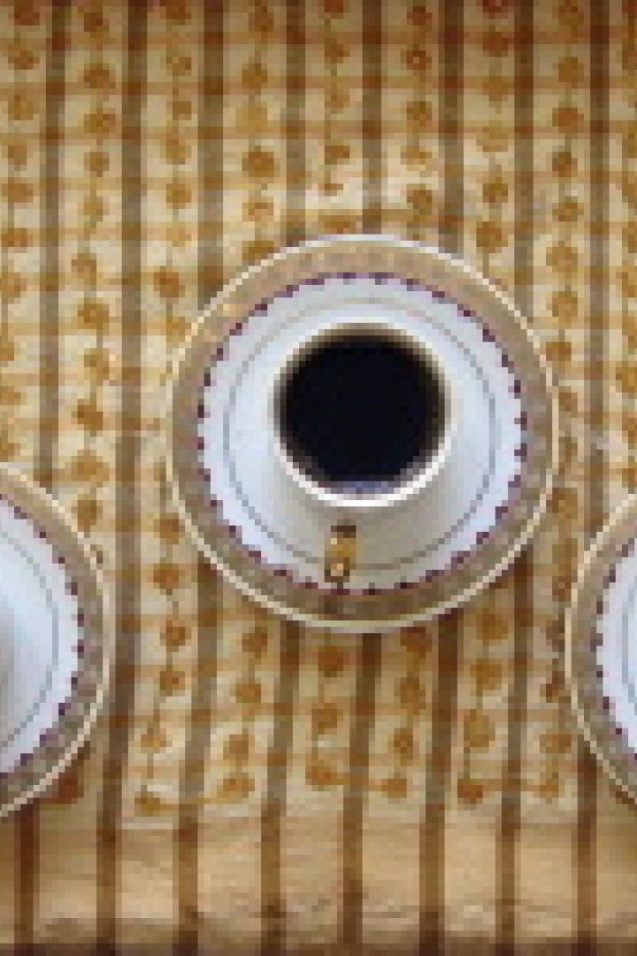 Drei Tassen Kaffee stehen auf einer gemusterten Tischdecke.