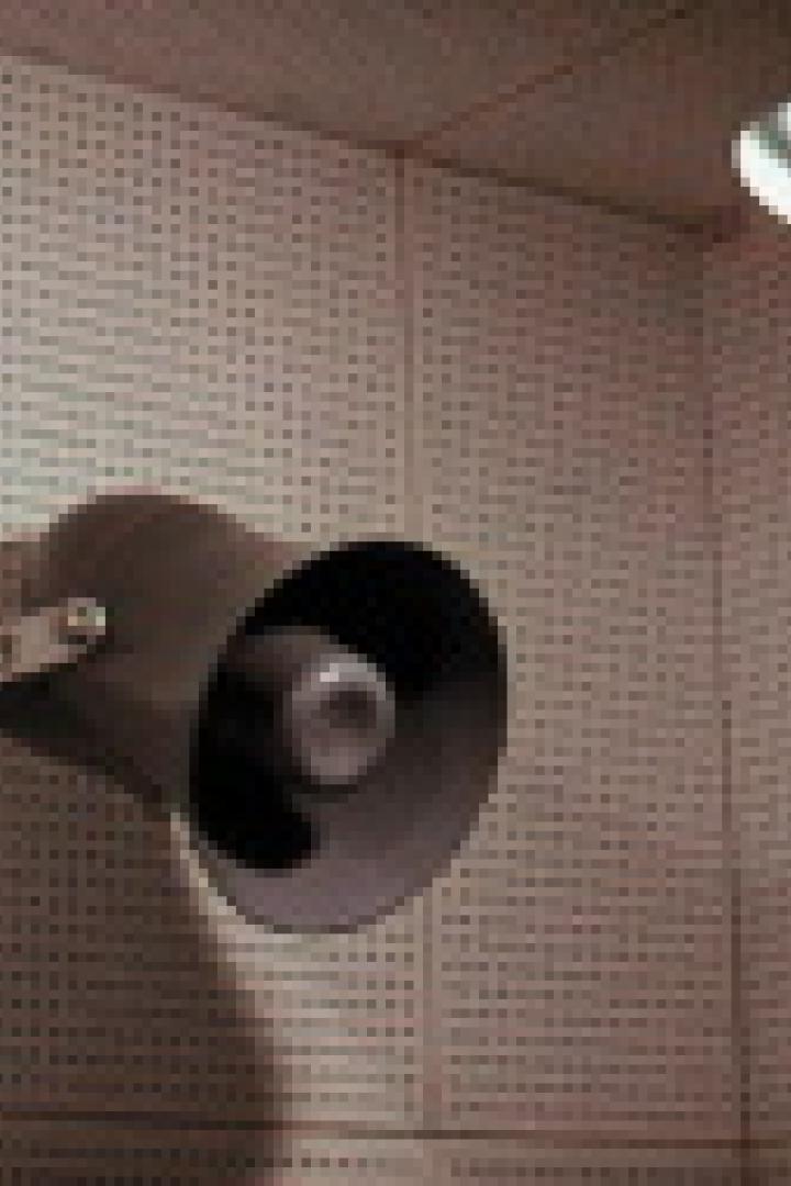 Ein grauer Lautsprecher hängt an einer Wand mit einer Weltkarte im Hintergrund.