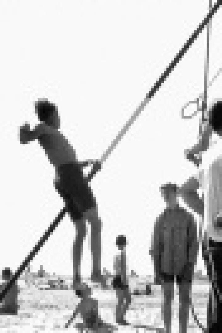 Eine Gruppe junger Männer turnt an einem improvisierten Reck auf einem sonnigen Strand.