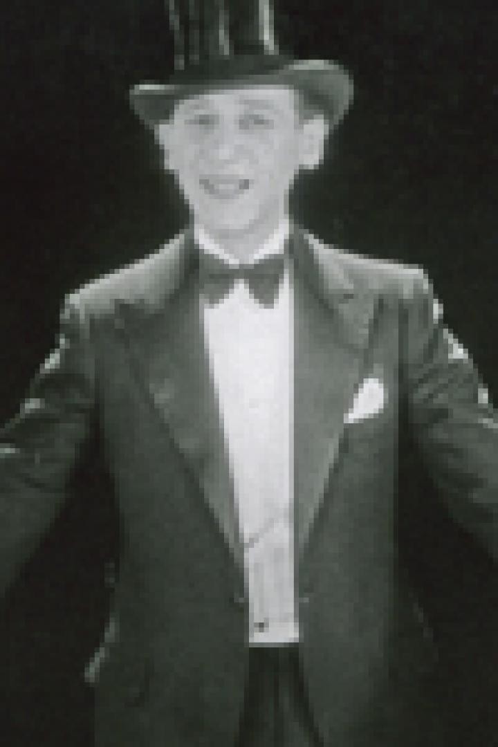 Ein Mann mit Zylinder, Anzug und Fliege singt oder spricht.