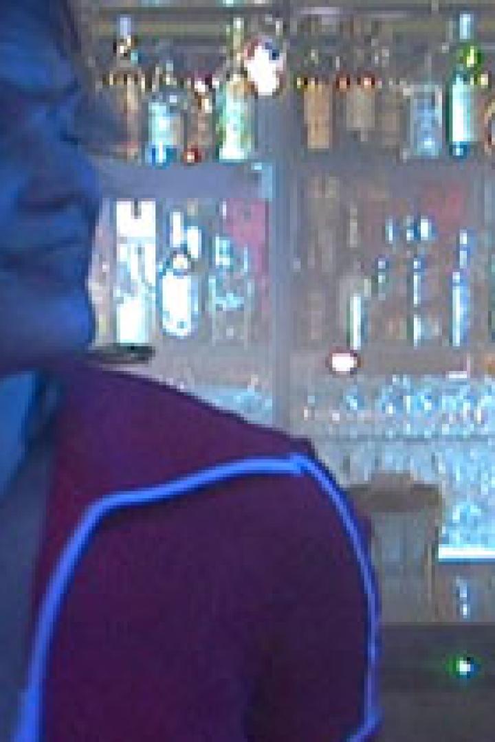 Eine Frau steht an einer Bar, während ein Barkeeper im Hintergrund arbeitet.