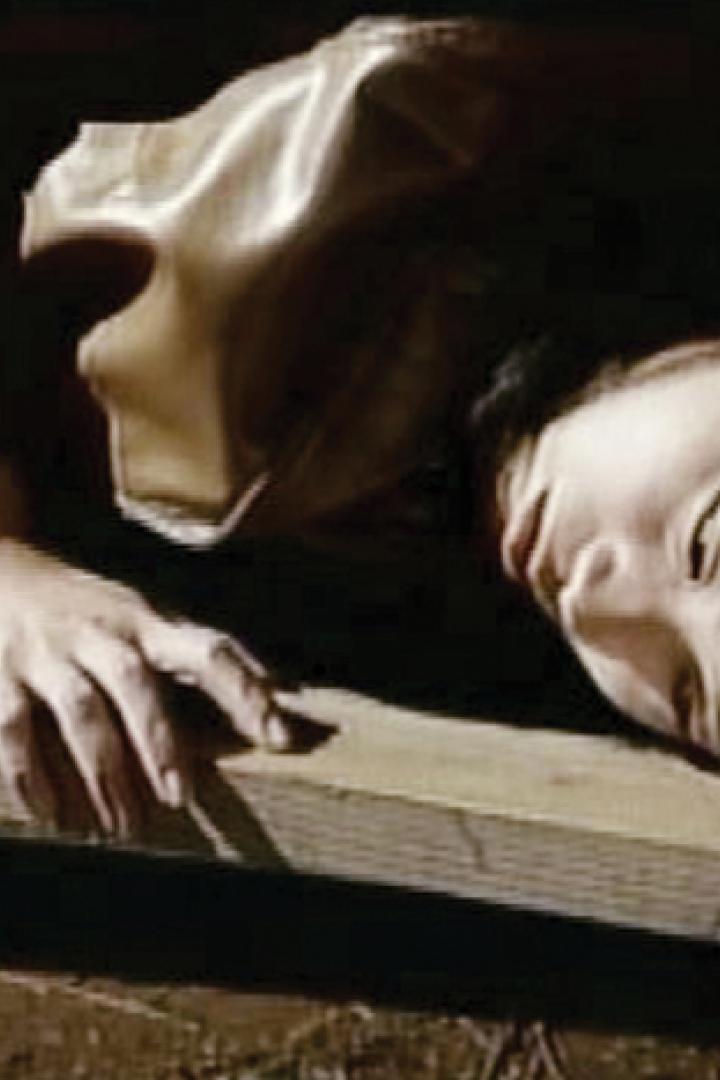 Eine verletzte Frau mit einem Verband liegt auf einem Holzbalken.