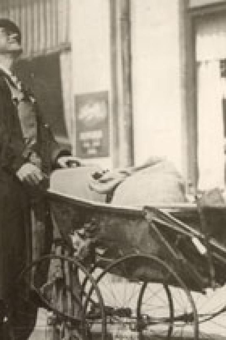 Ein Mann mit Hut schiebt einen Kinderwagen und blickt nach oben.