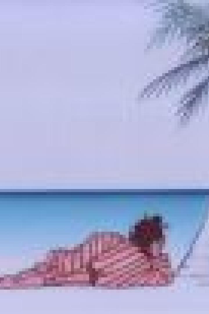 Eine Person liegt am Strand im Schatten einer Palme.