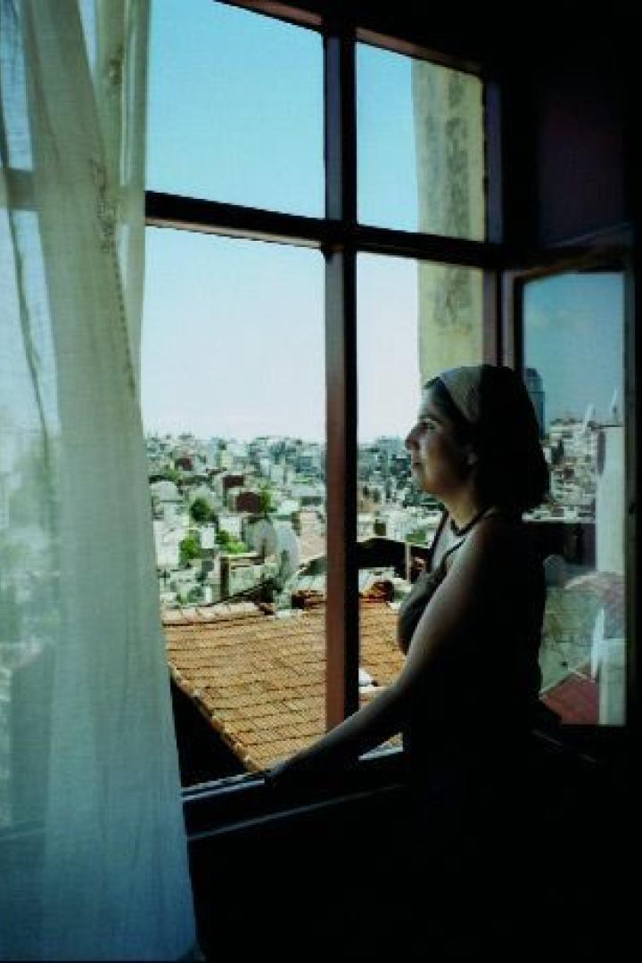 Eine Frau blickt aus einem Fenster auf eine Stadtlandschaft.