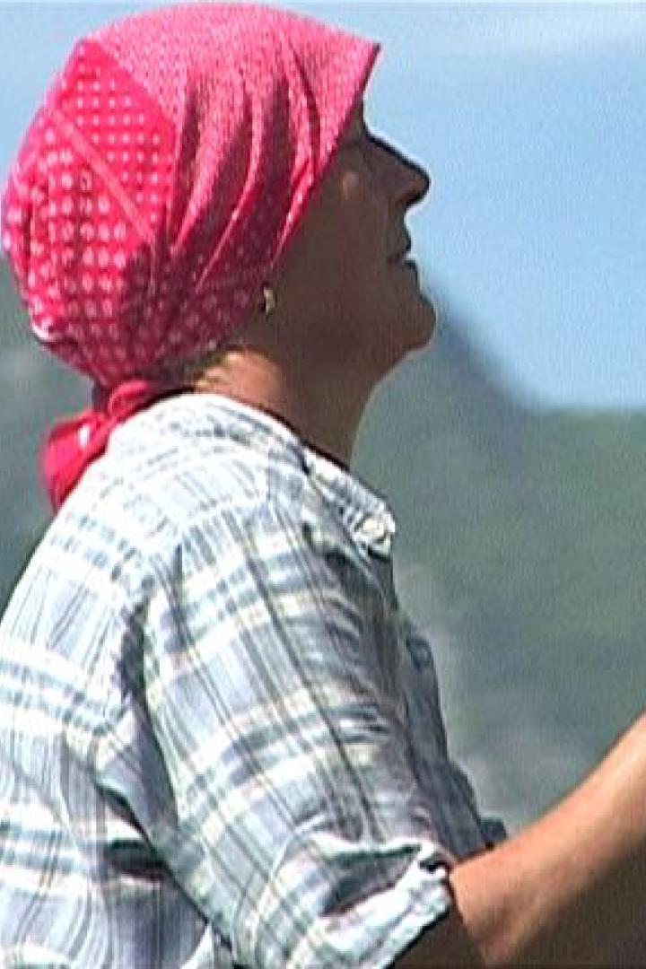 Eine Frau mit Kopftuch fährt einen Traktor vor einer Bergkulisse.