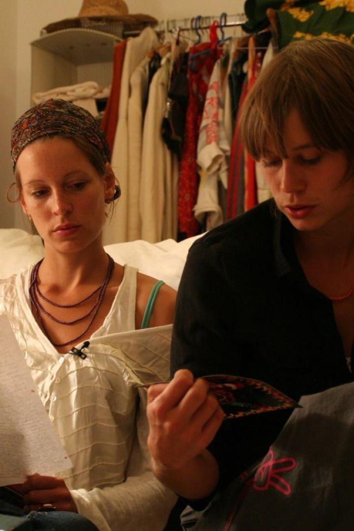 Zwei junge Frauen sitzen auf dem Boden und lesen einen Brief und eine Broschüre.