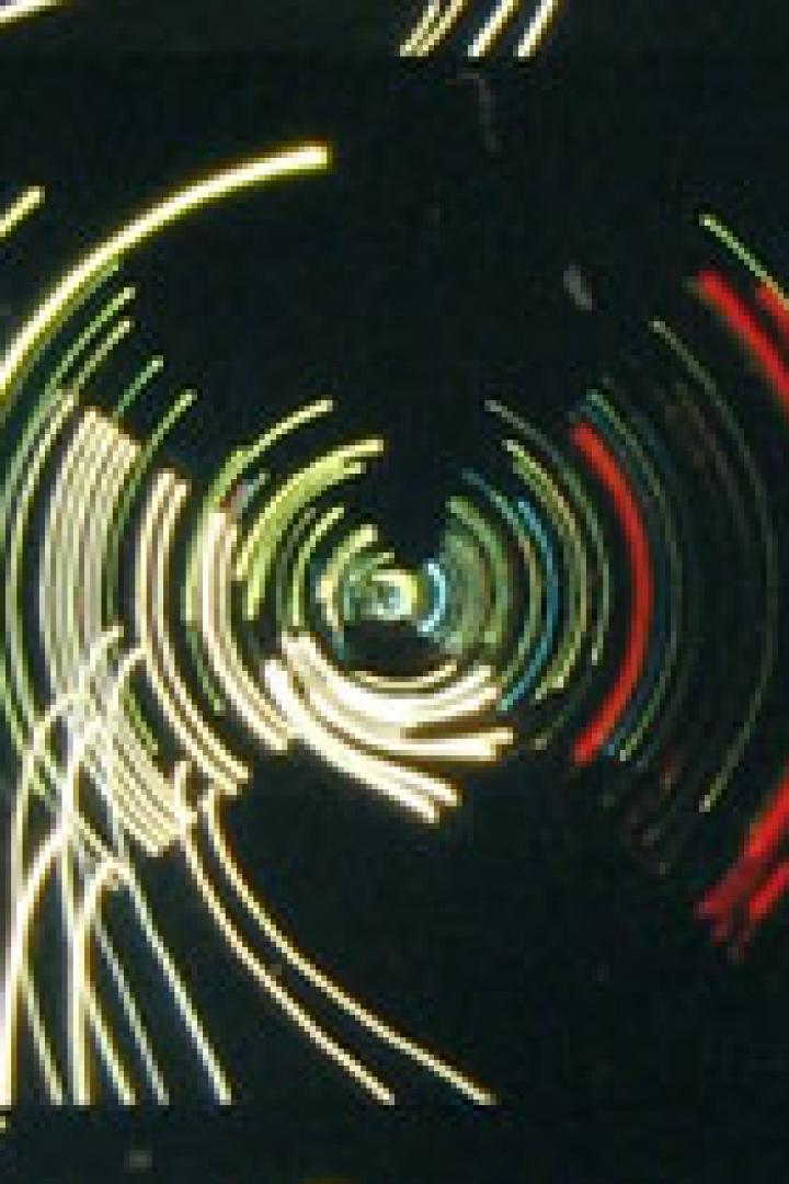 Kreisförmige Lichtspuren in Gelb, Rot und Blau auf schwarzem Hintergrund.