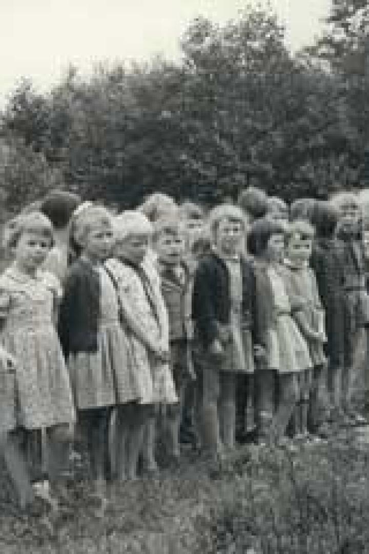 Eine Gruppe Kinder steht mit einem Mann in einer Reihe auf einer Wiese.