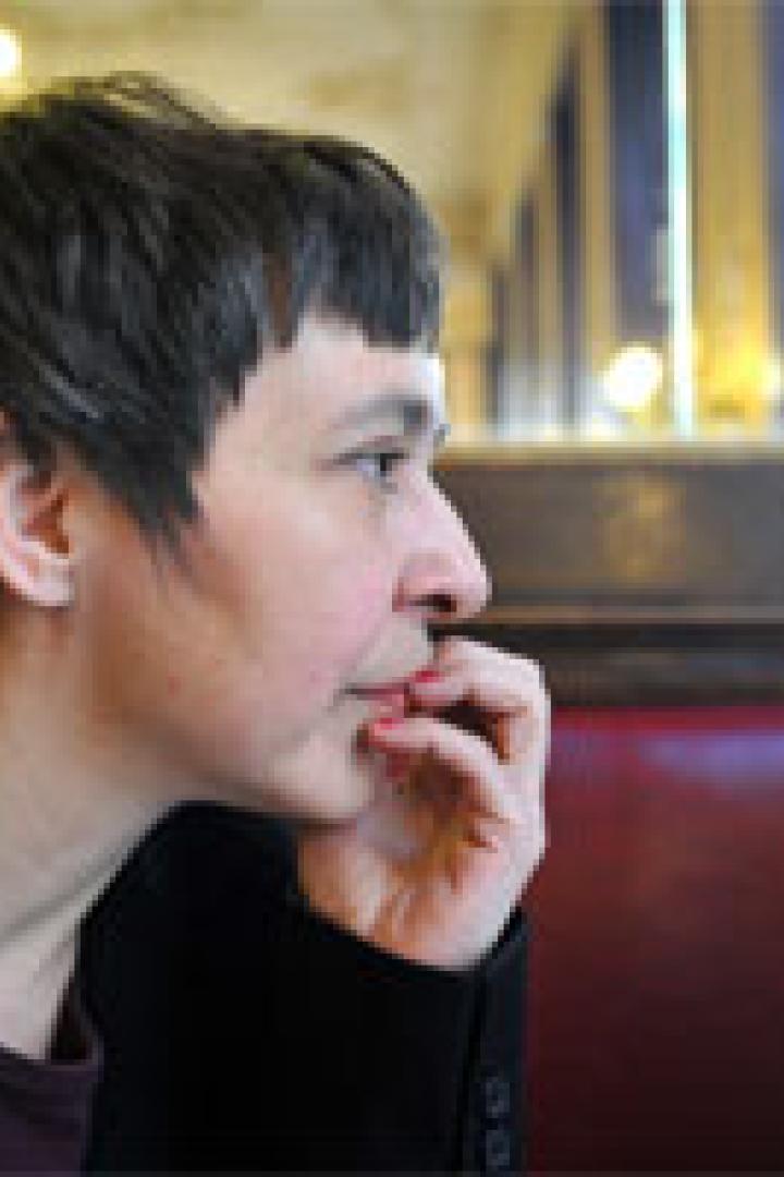 Eine Frau mit dunkler Jacke sitzt in einem Café und blickt nach rechts.