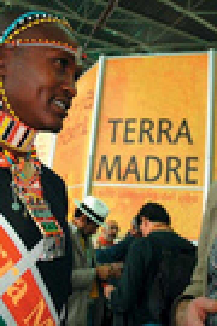 Ein Mann in traditioneller afrikanischer Kleidung spricht mit einem Mann in westlicher Kleidung vor einem „Terra Madre“-Schild.