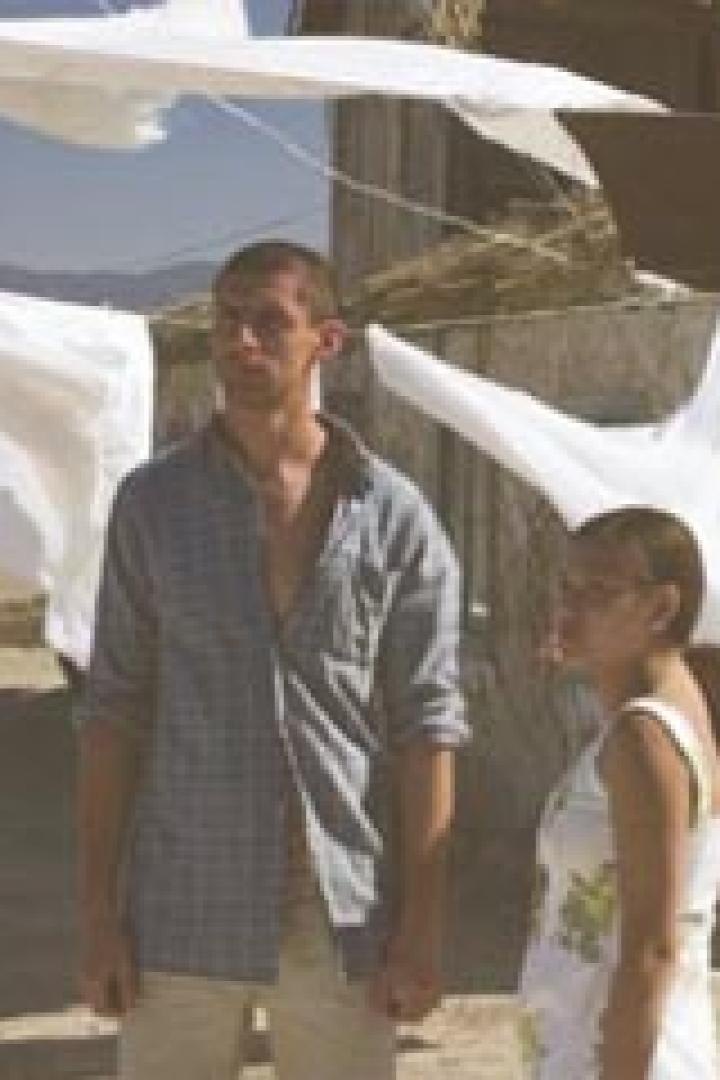 Ein junges Paar steht vor einem Haus, an dem Wäsche zum Trocknen aufgehängt ist.