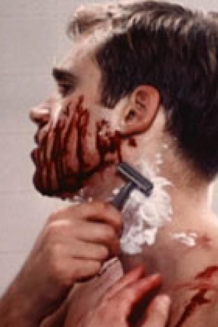 Ein Mann rasiert sich, sein Gesicht und Hals sind mit Blut bedeckt.