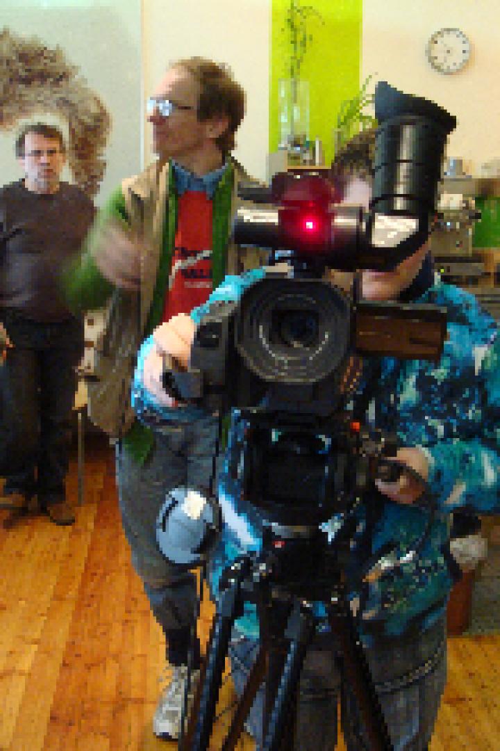 Eine Person filmt mit einer professionellen Videokamera in einem Raum, in dem sich mehrere Personen aufhalten.