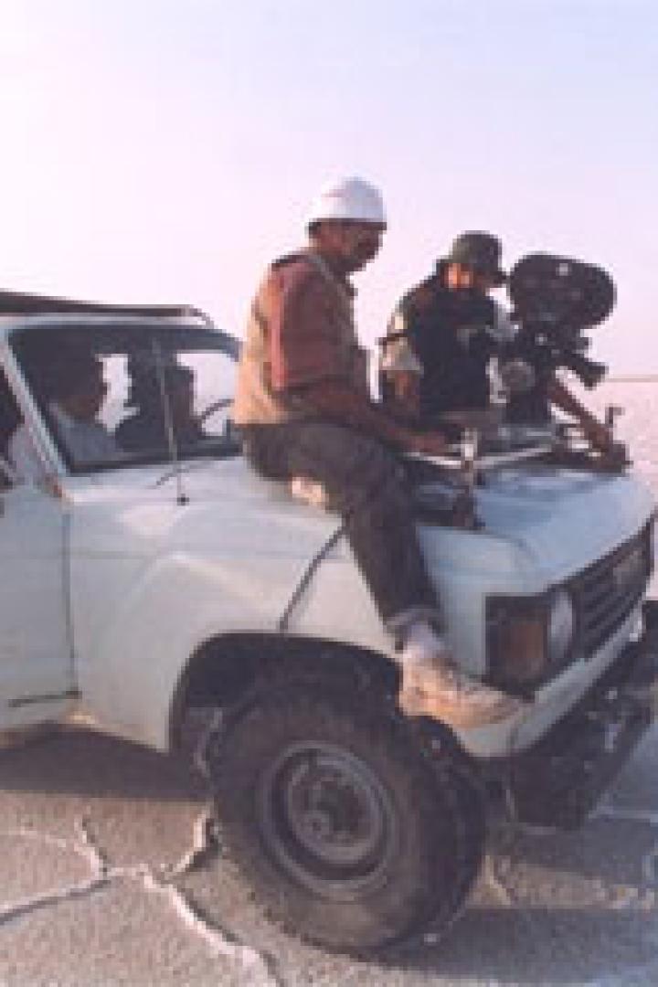 Zwei Männer mit Kamera auf einem Geländewagen in einer weiten, flachen Landschaft.