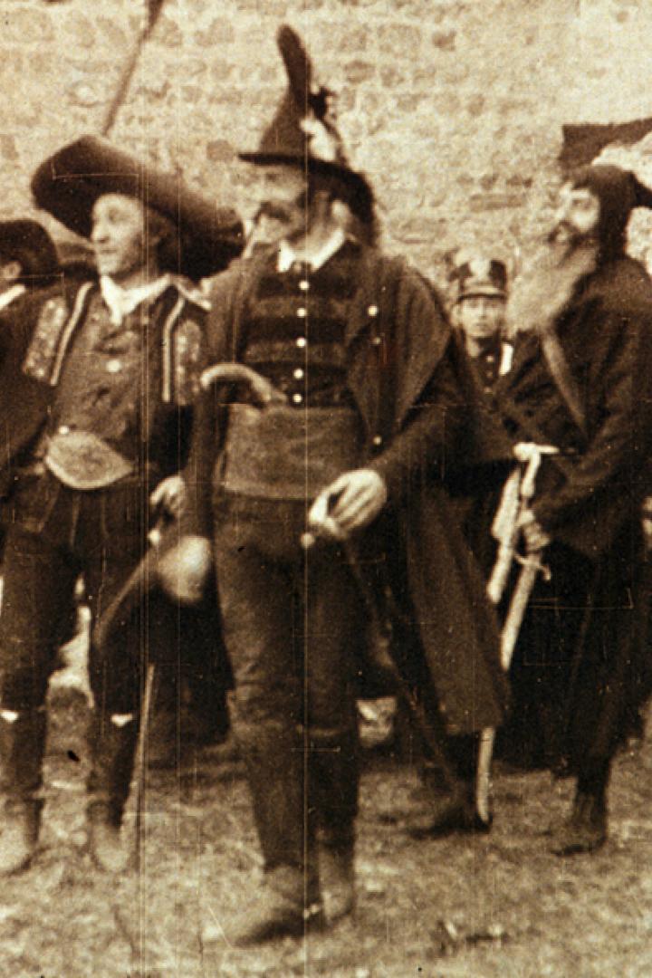 Eine Gruppe von Männern in Trachten steht vor einer Steinmauer.