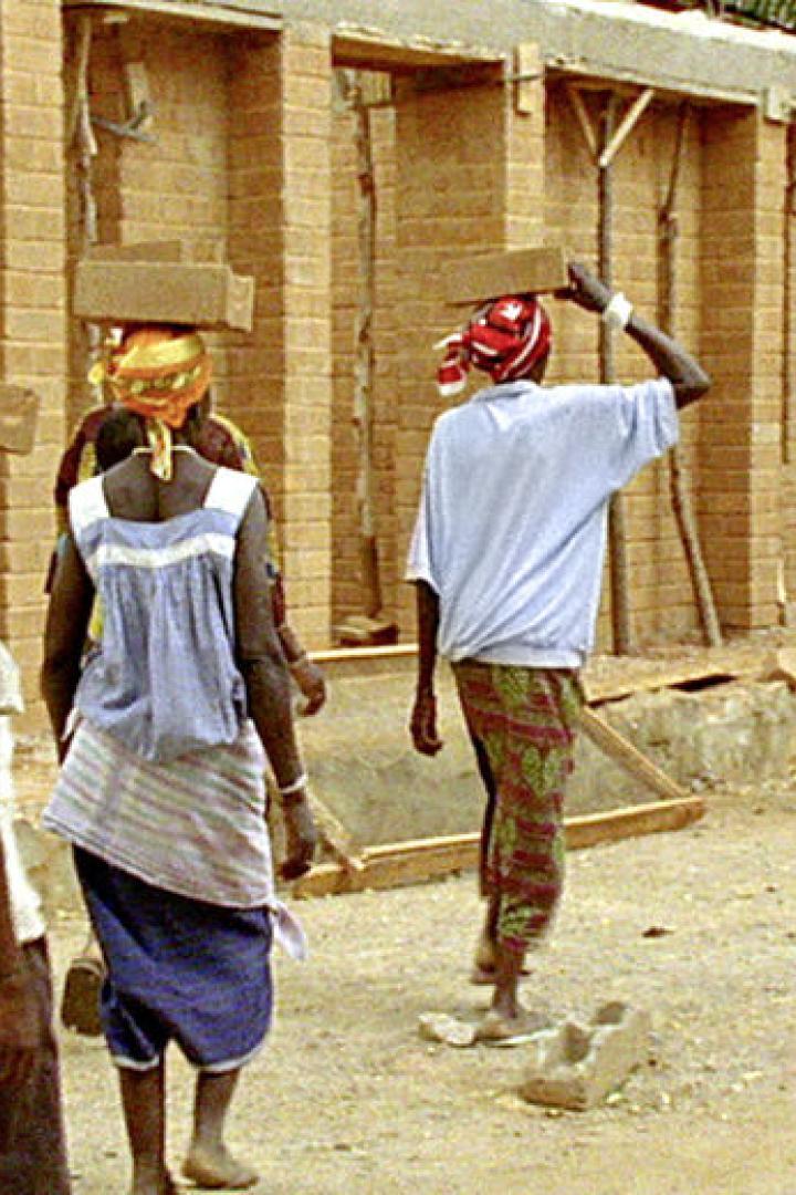 Frauen tragen Ziegelsteine auf ihren Köpfen zu einer Baustelle.