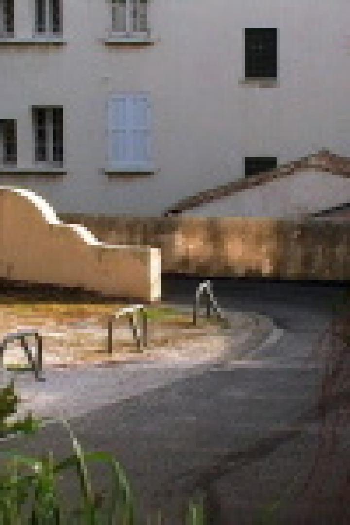 Ein asphaltierter Weg führt an einer Mauer und einem Gebäude vorbei.