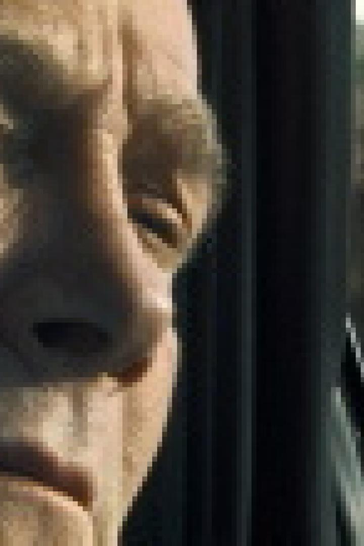 Ein Mann blickt ernst, während ein anderer im Autofenster zu sehen ist.