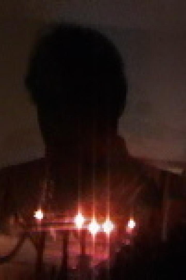 Eine Person steht im Dunkeln vor einer Reihe von Kerzen.