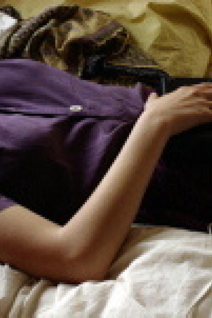 Eine Frau liegt mit einem Smartphone in der Hand auf einem Bett.