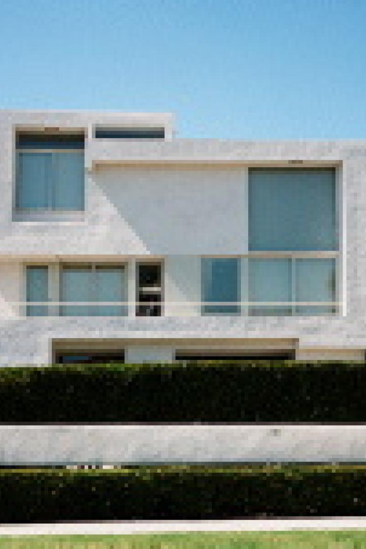 Ein modernes, weißes Haus mit großen Fenstern und einer grünen Hecke im Vordergrund.