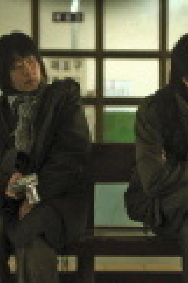 Zwei Männer sitzen auf einer Bank in einem Wartebereich und schauen in die Ferne.