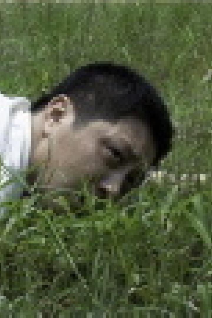 Ein Mann liegt im Gras und scheint etwas zu suchen.