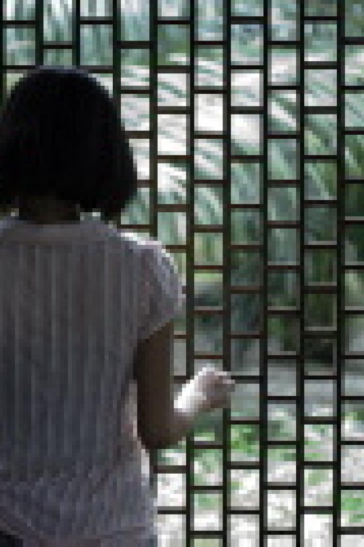 Eine Frau steht vor einem Fenster mit rechteckigen Glasbausteinen und blickt nach draußen.