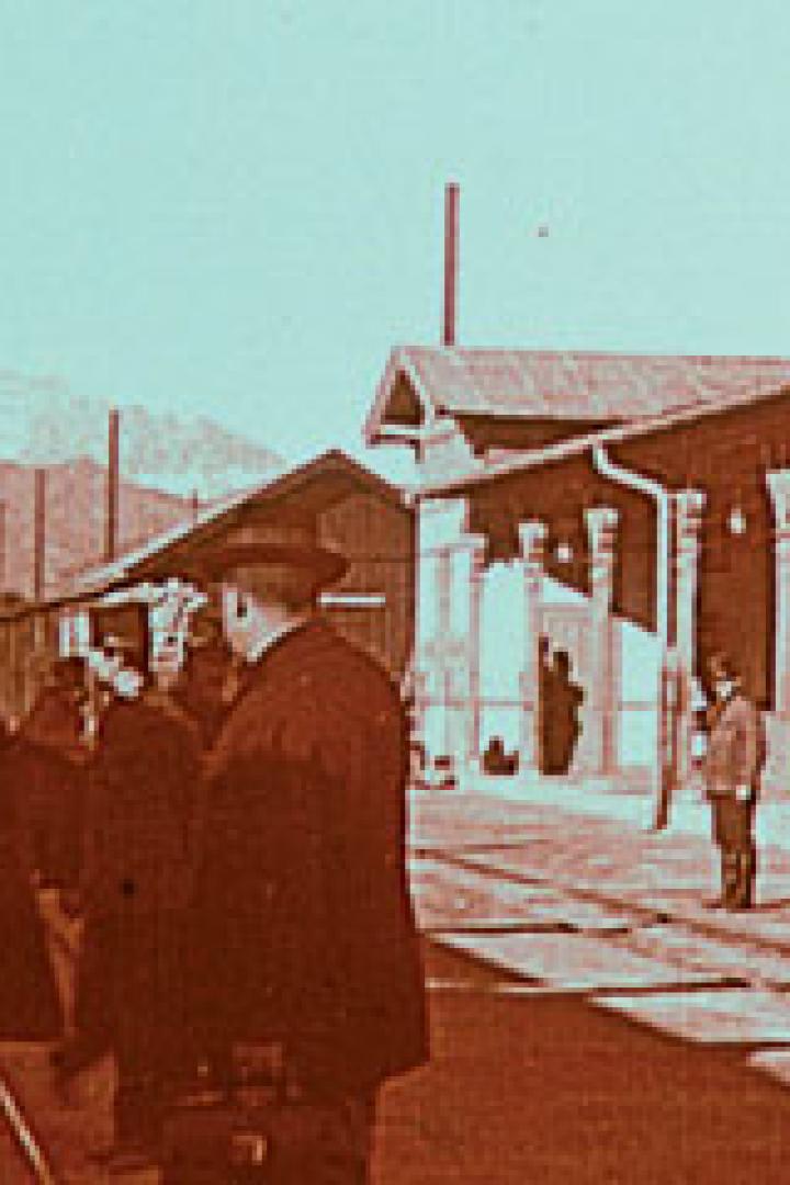 Eine Gruppe von Männern mit Hüten steht vor einem Bahnhofsgebäude.