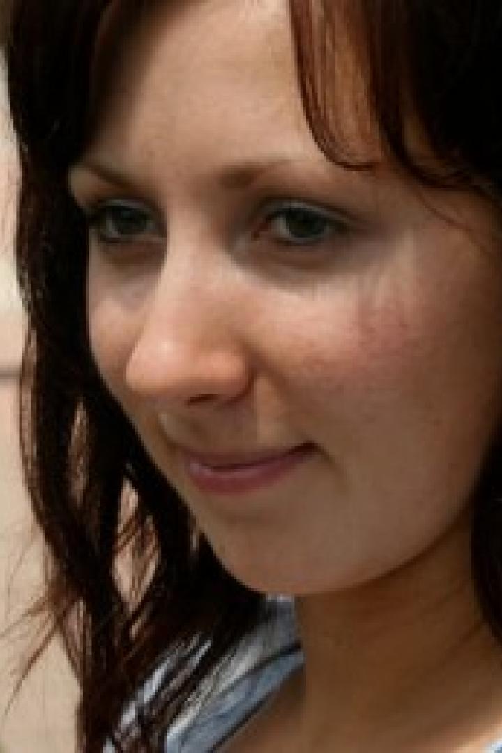 Eine junge Frau mit braunen Haaren lächelt leicht.