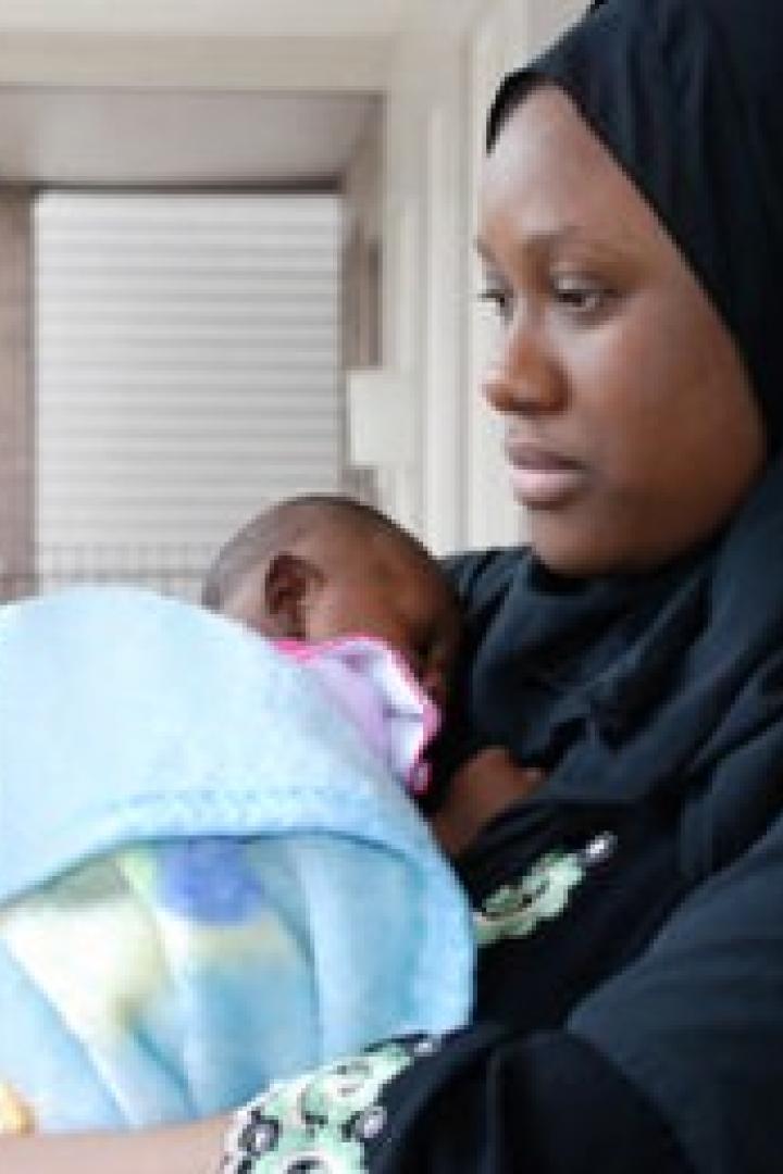 Eine Frau mit Hidschab hält ein in eine blaue Decke gewickeltes Baby.