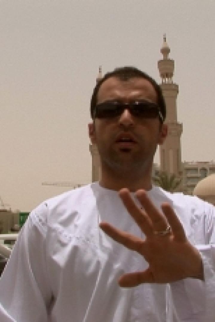 Ein Mann in traditioneller Kleidung steht vor einer Moschee und einem Parkplatz.